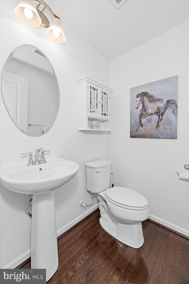 half bathroom with baseboards, wood finished floors, and toilet