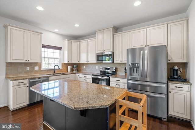kitchen with light stone counters, stainless steel appliances, a sink, decorative backsplash, and a kitchen bar