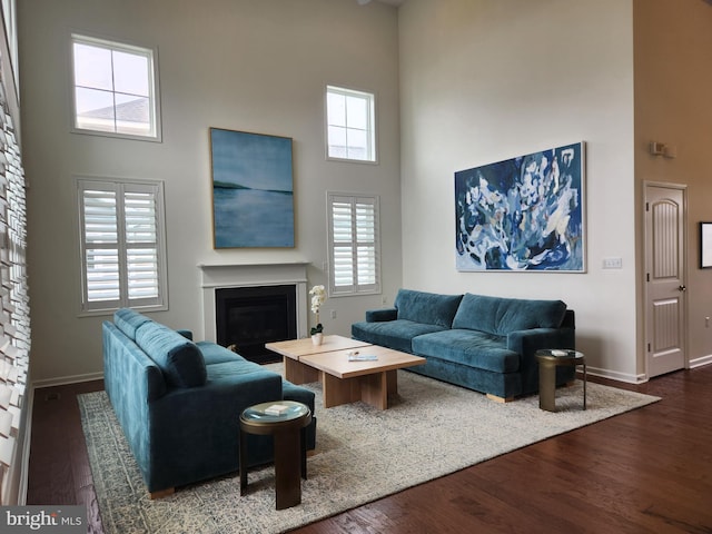 living area featuring baseboards, a high ceiling, dark wood-type flooring, and a glass covered fireplace