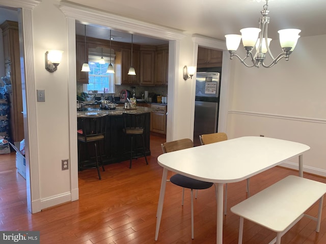 kitchen with decorative backsplash, a breakfast bar, freestanding refrigerator, an inviting chandelier, and light wood finished floors