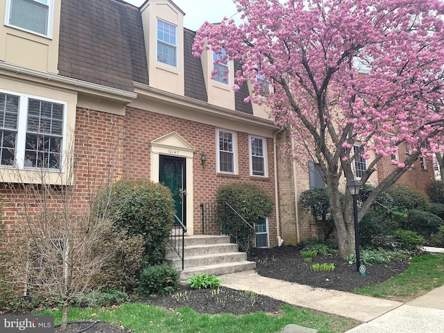 view of front of home with brick siding, a shingled roof, and mansard roof