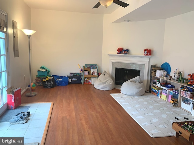 living area with wood finished floors, ceiling fan, electric panel, and a fireplace