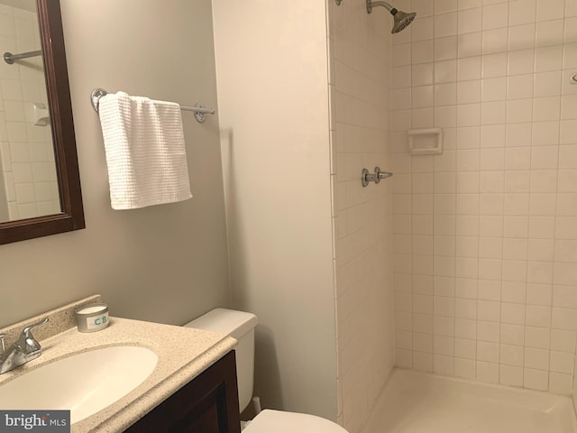 full bathroom with toilet, a tile shower, and vanity