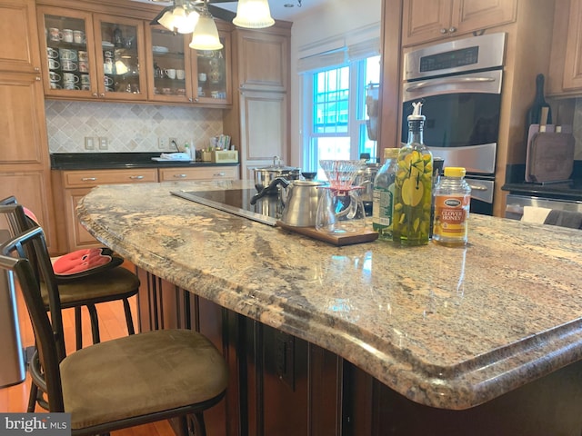 kitchen featuring glass insert cabinets, dark stone countertops, a breakfast bar area, backsplash, and double oven