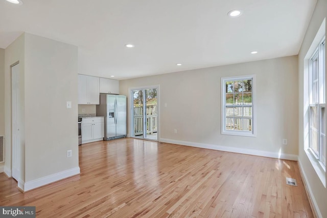 unfurnished living room featuring baseboards, plenty of natural light, light wood-style flooring, and visible vents