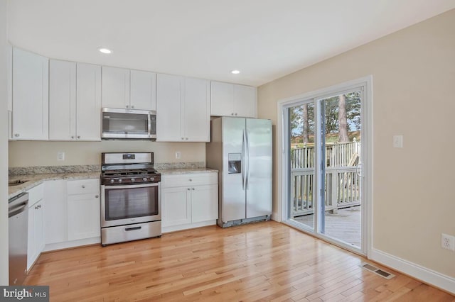 kitchen with visible vents, appliances with stainless steel finishes, light stone countertops, white cabinets, and light wood finished floors
