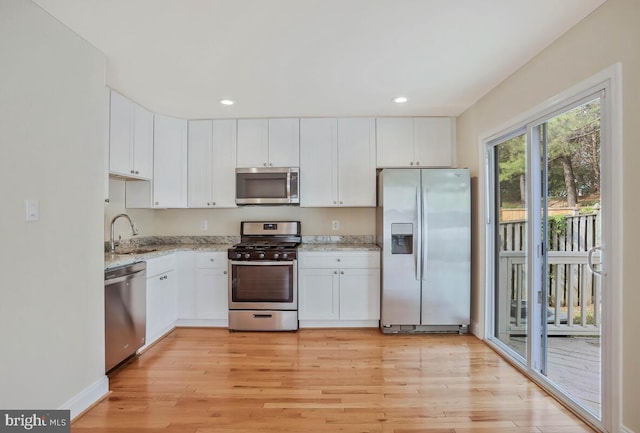 kitchen featuring light stone counters, appliances with stainless steel finishes, a sink, and light wood-type flooring