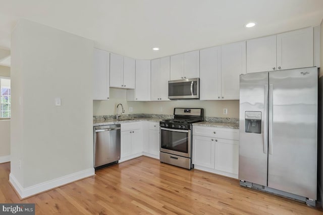 kitchen with light stone countertops, a sink, light wood-style floors, stainless steel appliances, and baseboards