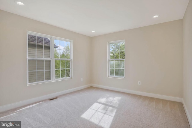 unfurnished room with light colored carpet, baseboards, visible vents, and plenty of natural light