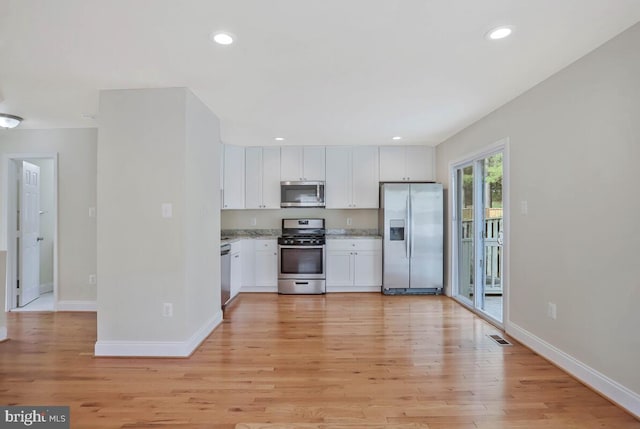 kitchen with white cabinets, stainless steel appliances, baseboards, and light wood-style floors
