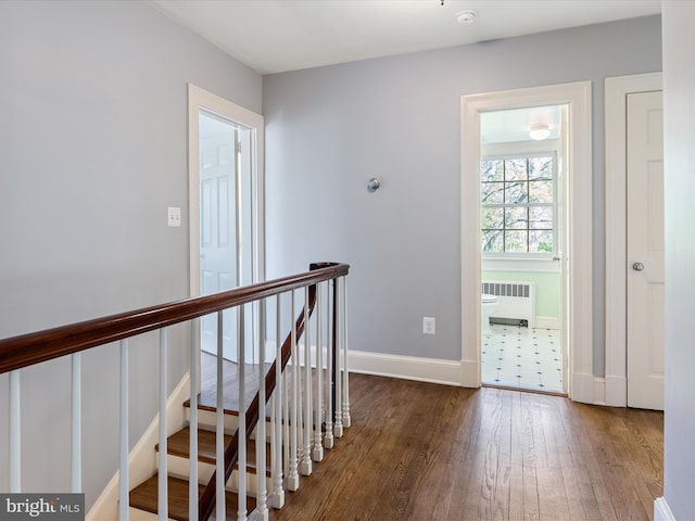 hall with baseboards, radiator, wood finished floors, and an upstairs landing