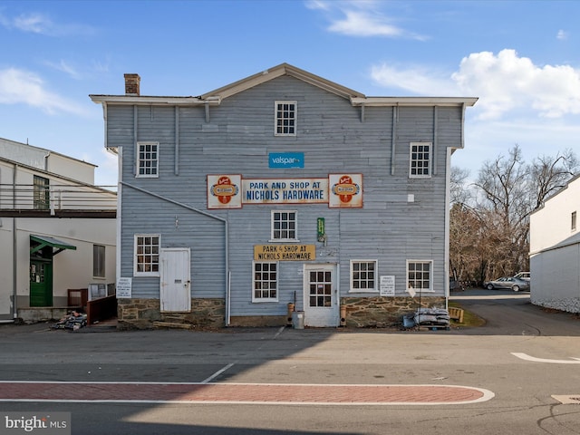 back of property with uncovered parking, a chimney, and stone siding