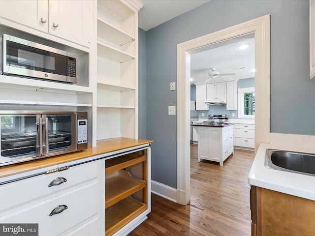 kitchen featuring dark wood-style flooring, open shelves, stainless steel appliances, white cabinetry, and a ceiling fan