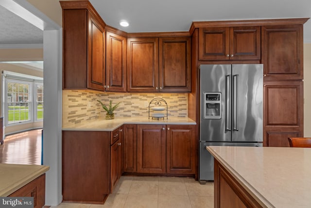 kitchen featuring light countertops, high end refrigerator, light tile patterned floors, backsplash, and ornamental molding