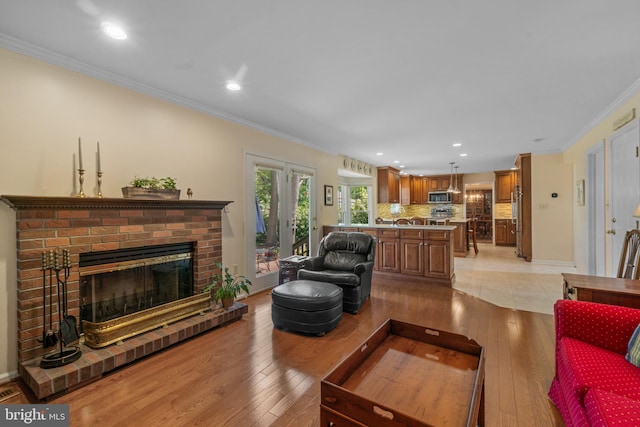 living room featuring crown molding, light wood finished floors, a brick fireplace, recessed lighting, and baseboards