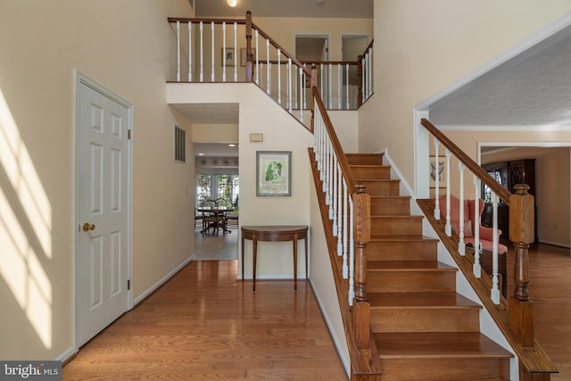 stairway featuring baseboards, a high ceiling, and wood finished floors