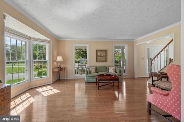 living area featuring a textured ceiling, crown molding, wood finished floors, baseboards, and stairs