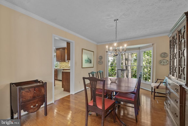 dining area with light wood-type flooring, ornamental molding, baseboards, and an inviting chandelier
