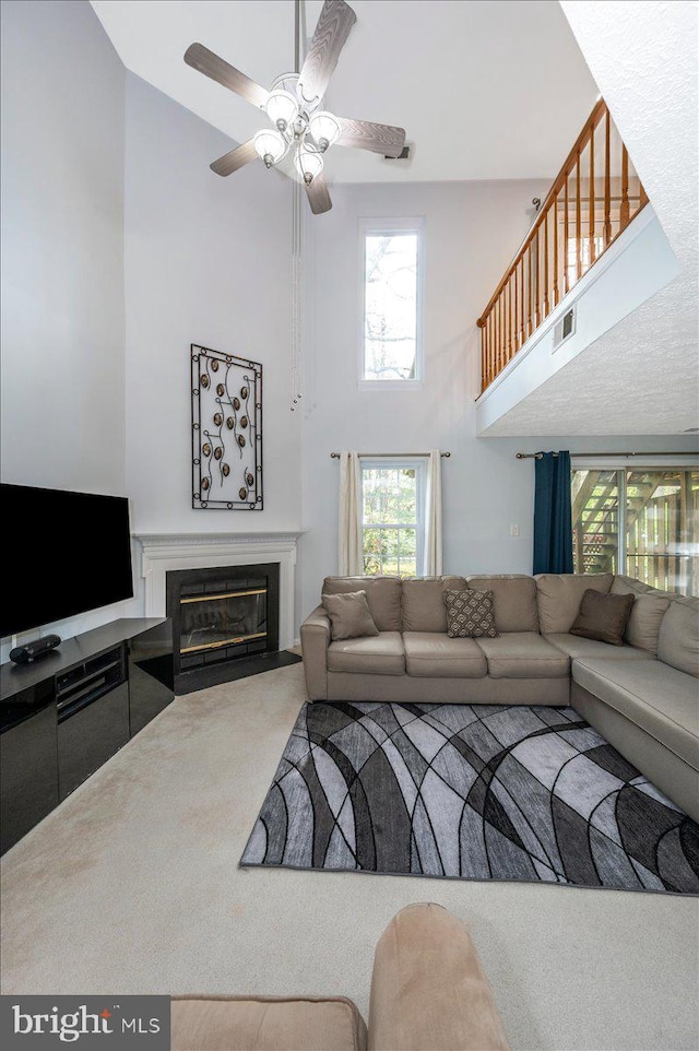 carpeted living room with a fireplace with flush hearth, a towering ceiling, visible vents, and ceiling fan