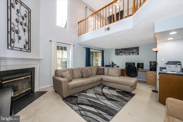 living room with a fireplace with flush hearth, light colored carpet, visible vents, baseboards, and a high ceiling