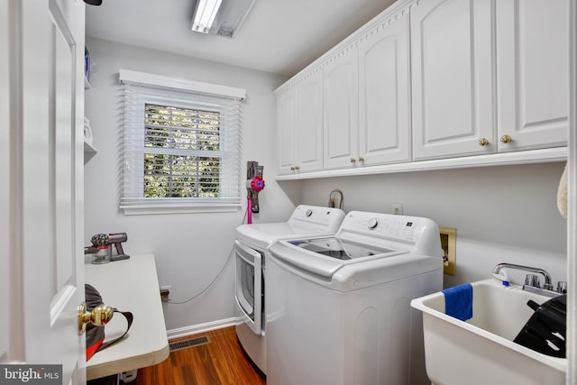 washroom with dark wood finished floors, washer and dryer, cabinet space, a sink, and baseboards