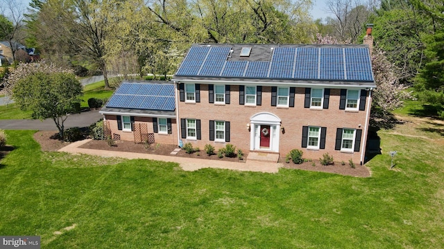 colonial-style house with roof mounted solar panels, a chimney, a front yard, and brick siding