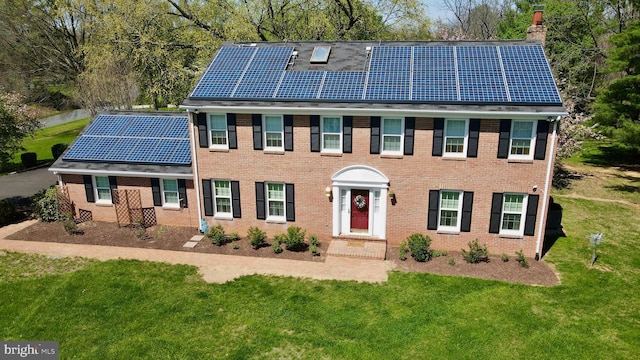 colonial house with a chimney, brick siding, solar panels, and a front lawn