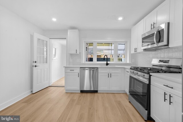 kitchen featuring white cabinets, a sink, light wood-style floors, tasteful backsplash, and appliances with stainless steel finishes