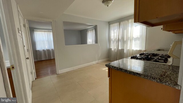 kitchen featuring baseboards, dark stone countertops, stove, and a healthy amount of sunlight
