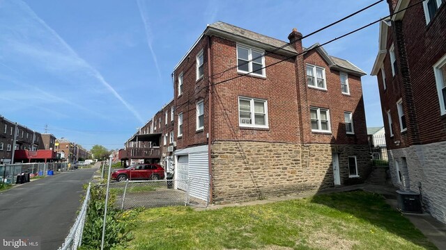 view of property exterior featuring central AC unit, fence, an attached garage, stone siding, and brick siding