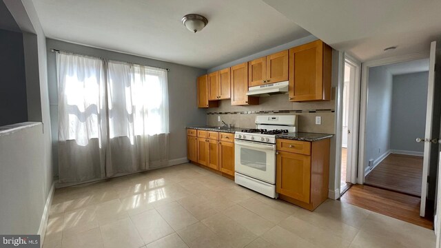 kitchen with gas range gas stove, dark stone counters, baseboards, under cabinet range hood, and light tile patterned floors