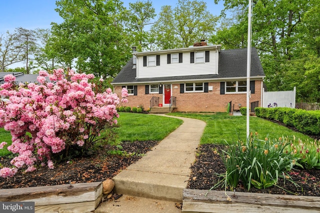 view of front of property featuring brick siding, roof with shingles, a front yard, and a chimney