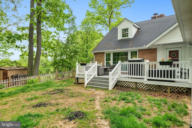 rear view of property featuring brick siding, a fenced backyard, roof with shingles, and a deck