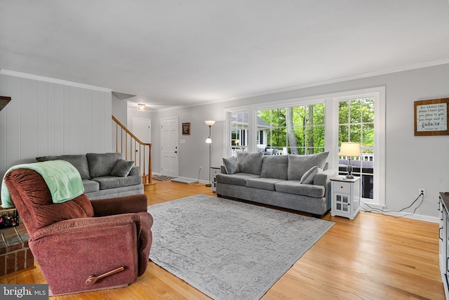 living room featuring baseboards, ornamental molding, light wood finished floors, and stairs