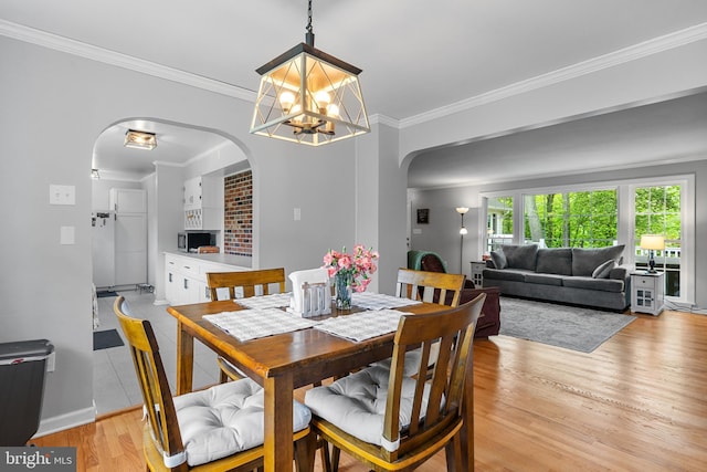 dining area featuring an inviting chandelier, light wood finished floors, arched walkways, baseboards, and ornamental molding