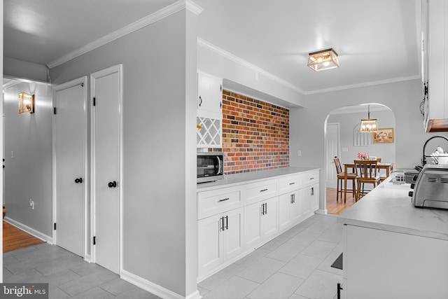 kitchen featuring crown molding, light countertops, white cabinetry, stainless steel microwave, and arched walkways