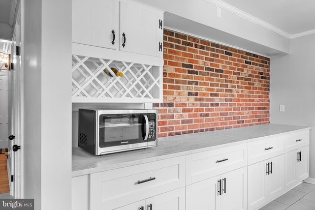 interior details with crown molding, light stone counters, stainless steel microwave, and white cabinetry