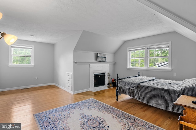 bedroom featuring a textured ceiling, a fireplace with flush hearth, wood finished floors, baseboards, and lofted ceiling