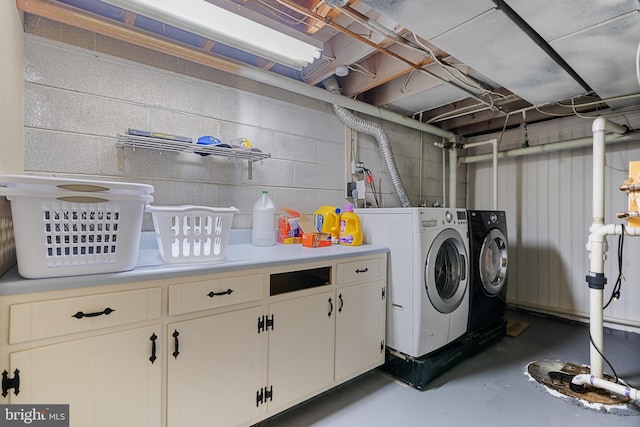 clothes washing area with concrete block wall, washing machine and dryer, and cabinet space