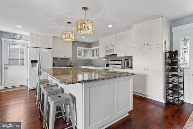 kitchen with white cabinets, backsplash, white appliances, a kitchen island, and dark wood-type flooring