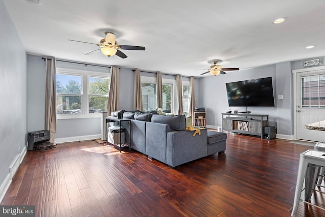 living room featuring recessed lighting, wood finished floors, a wood stove, a ceiling fan, and baseboards