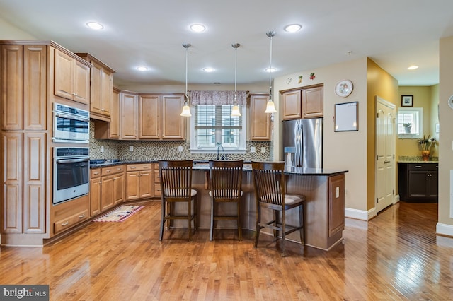 kitchen with light wood finished floors, a kitchen bar, a center island, backsplash, and appliances with stainless steel finishes