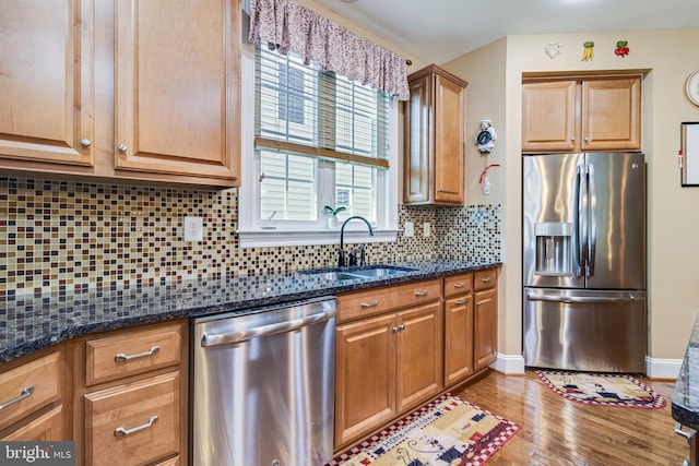 kitchen with a sink, dark stone countertops, tasteful backsplash, light wood-type flooring, and appliances with stainless steel finishes