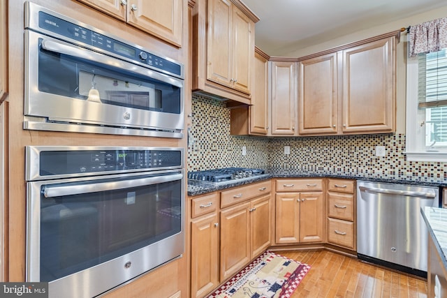 kitchen with backsplash, appliances with stainless steel finishes, light wood finished floors, and dark stone counters