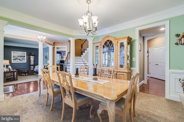carpeted dining space featuring stairway, a chandelier, ornamental molding, ornate columns, and wood finished floors
