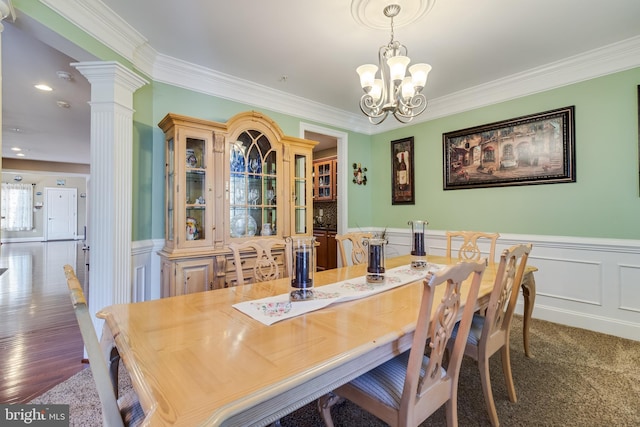 dining space with ornate columns, crown molding, a notable chandelier, and wainscoting