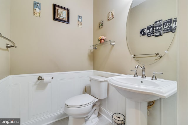 bathroom featuring a sink, a wainscoted wall, toilet, and a decorative wall