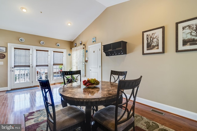 dining space featuring wood finished floors, visible vents, high vaulted ceiling, and baseboards