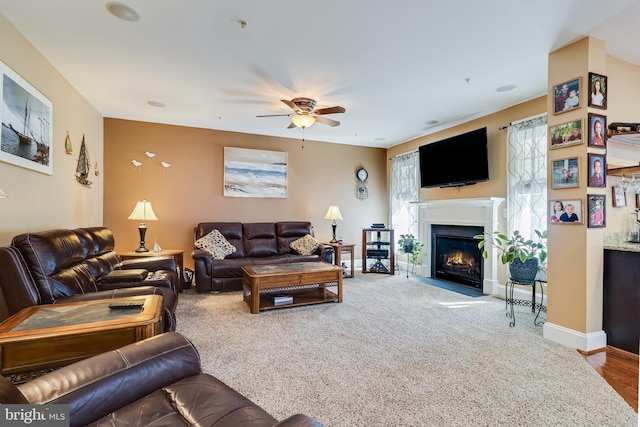 living area with a ceiling fan, a fireplace with flush hearth, carpet floors, and baseboards