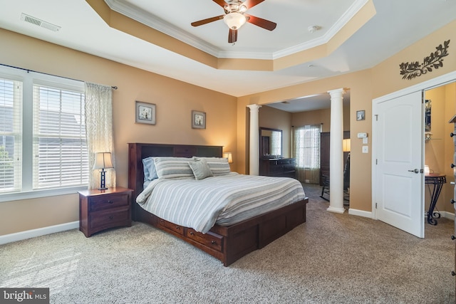bedroom with carpet flooring, visible vents, a tray ceiling, ornamental molding, and decorative columns